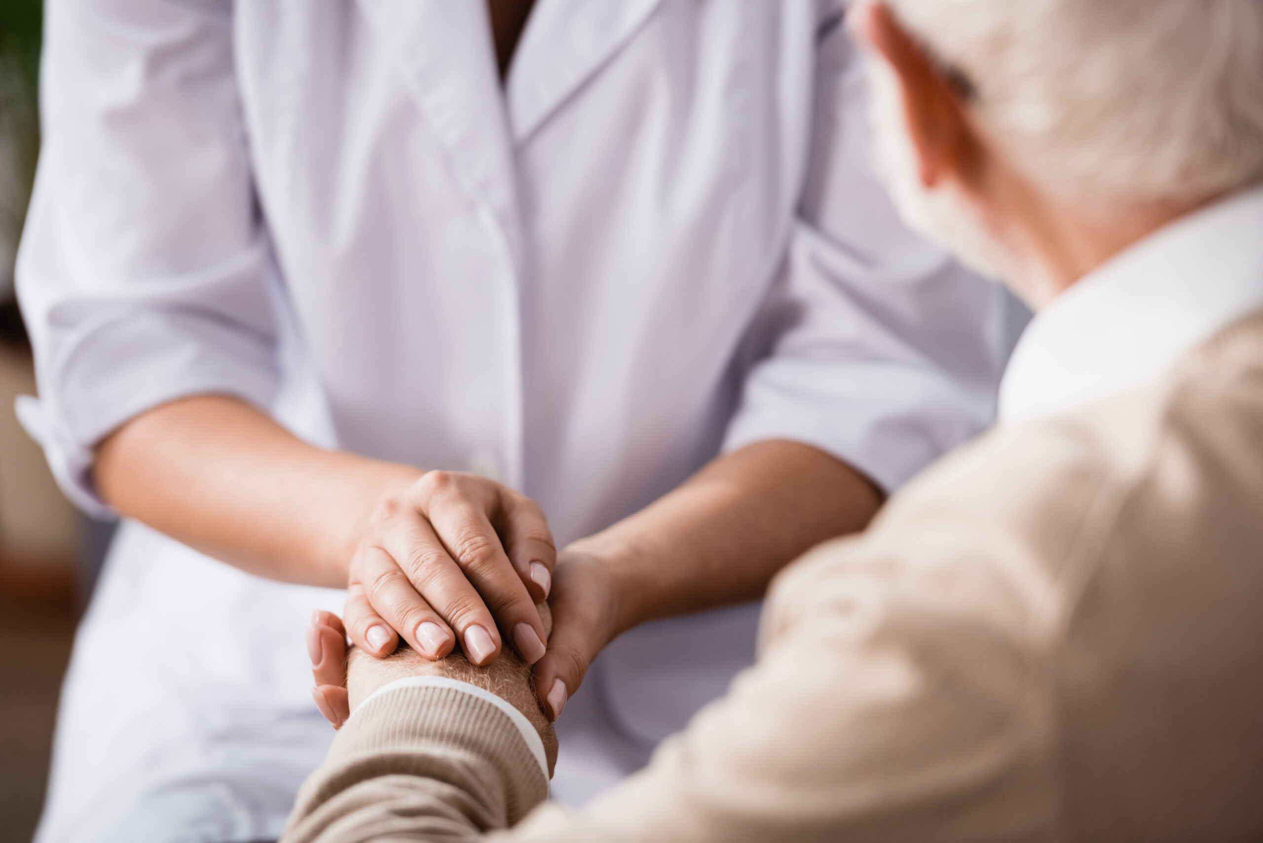 cropped view of social worker holding hands of aged man on blurr